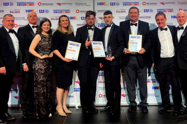 A group photo at an awards ceremony of nine people dressed in black suits and dresses, standing in a line. Three of them are holding plaques and award statuettes.