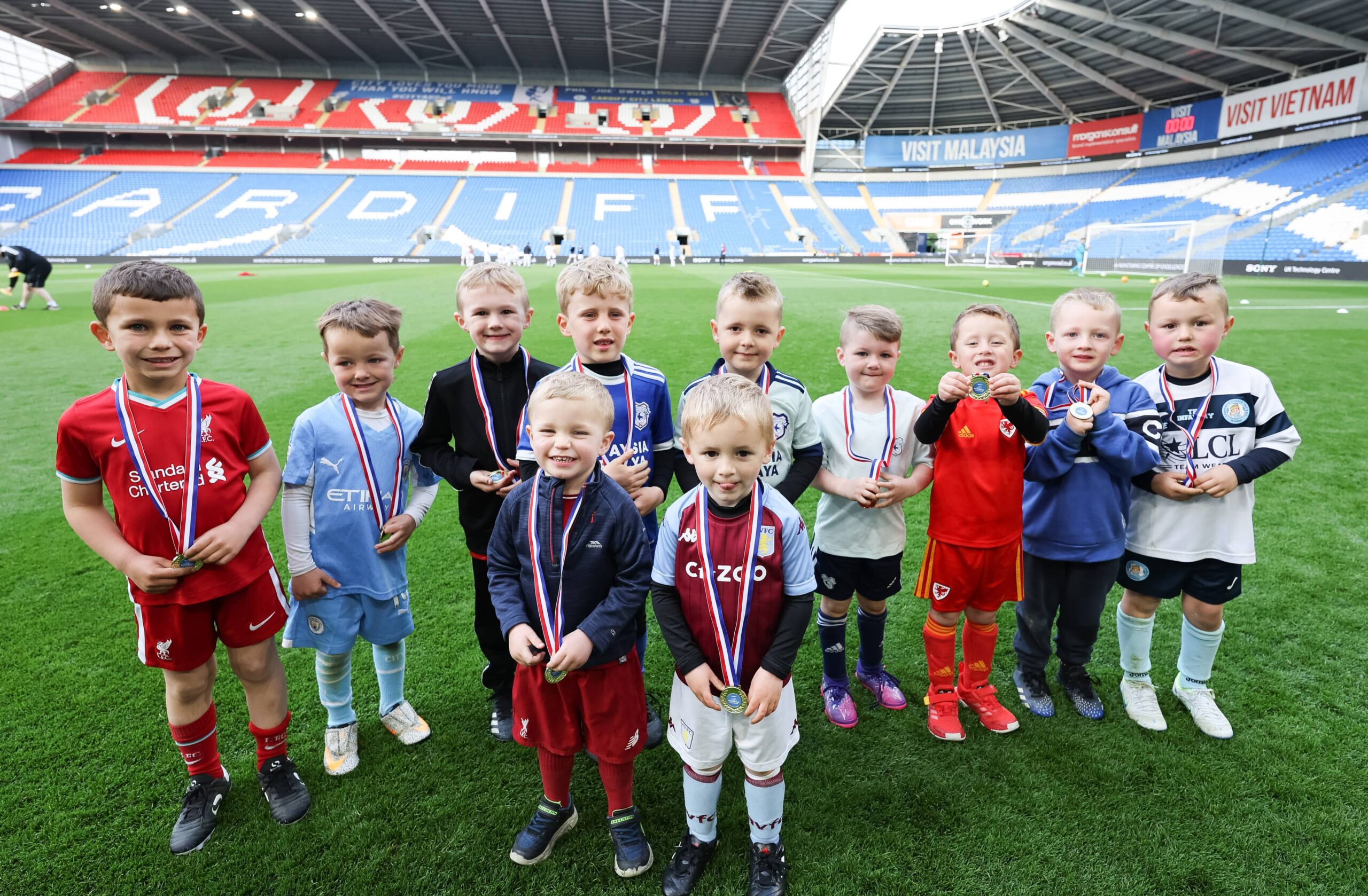 A photo of a small group of children standing on the pitch of Cardiff City Football Club Stadium wearing medals for participating in a Sony Charity Football children's game.