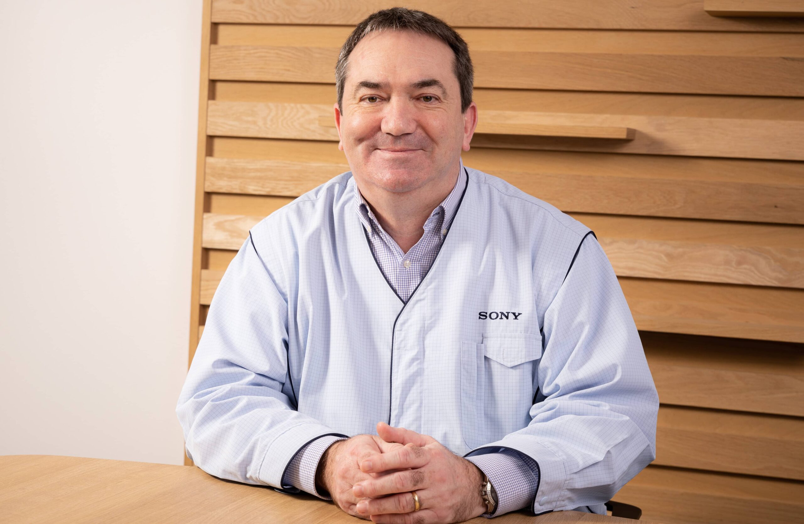 A man with black hair wearing a Sony uniform, sitting at a wooden table.