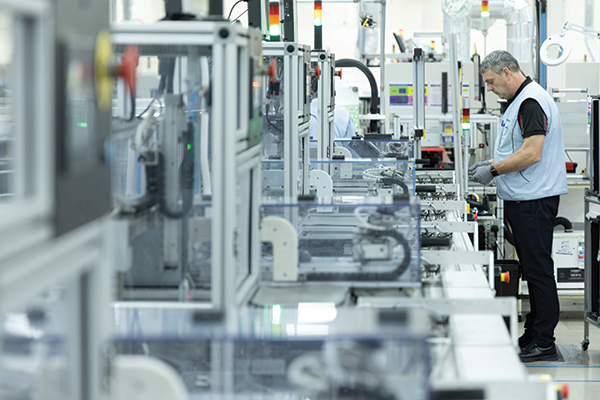 A photo of various manufacturing machines lined up in a row. To the right of them, a man wearing a Sony uniform is doing work.