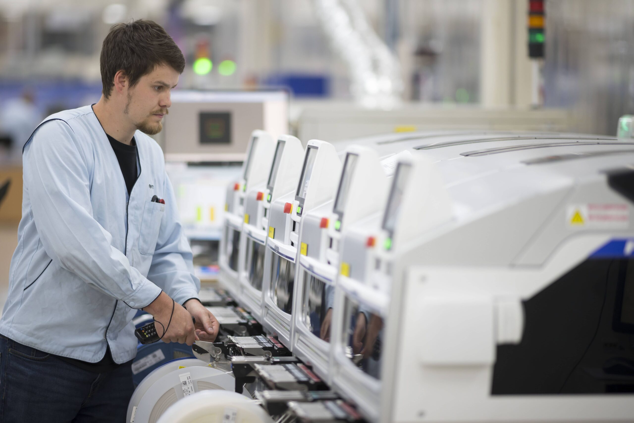 A photo of an Surface Mount Technology manufacturing process. On the left-hand side is a man in a Sony uniform, working. On the right is a row of white machines.