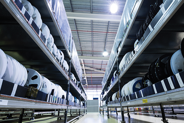 A photo of a warehouse space. In the middle of a photo is a walkway, and on either side of it are racks of parts