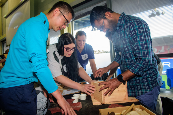 A photo of three men of various ethnicities and a woman working together on a wooden bird box.