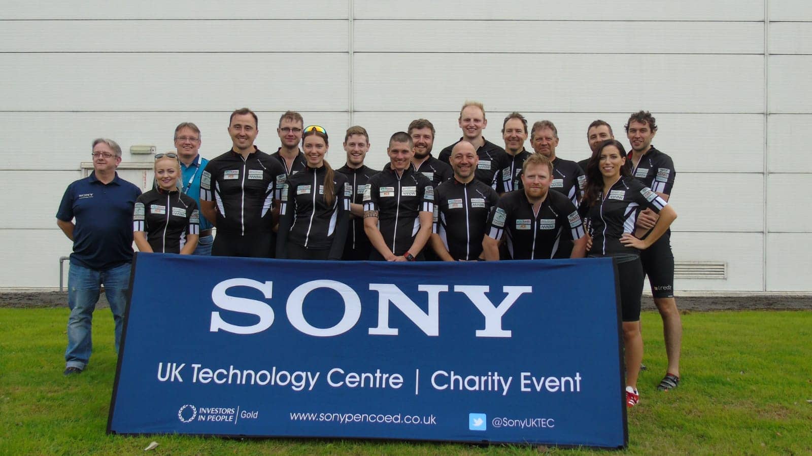 A group of Sony UK TEC employees dressed in biking gear standing behind a blue banner with the text 'Sony UK Technology Centre Charity Event'